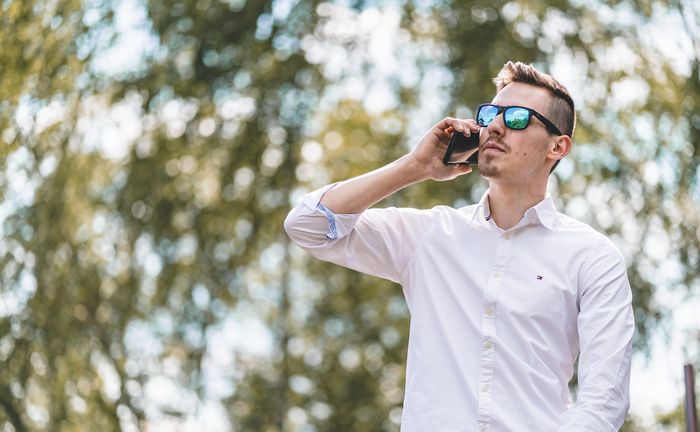 A man in a white shirt is standing outside talking on his cell phone.