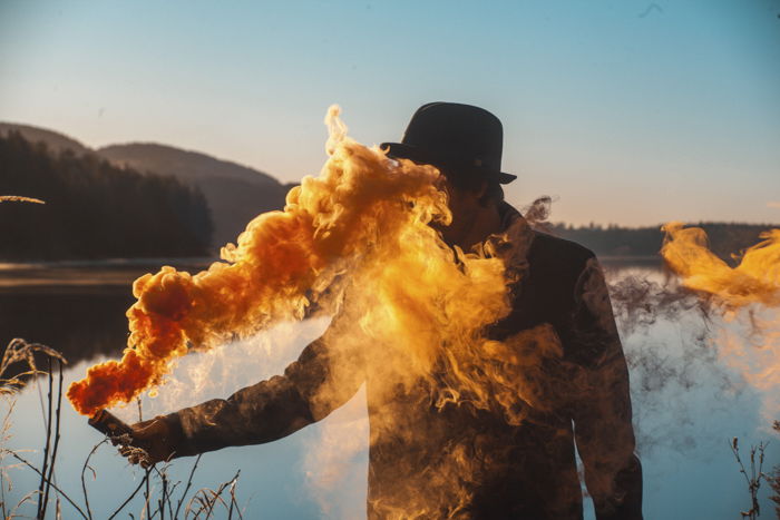 A man holding a smoke grenade emitting bright yellow smoke in front of a landscape