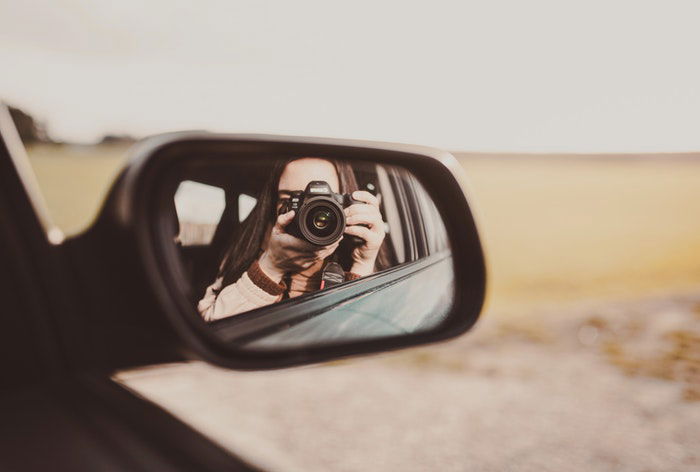 A girl taking a self portrait in a car side mirror