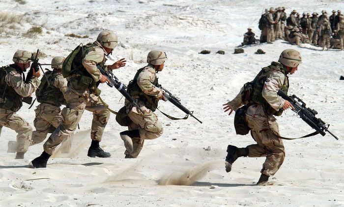 a photo of military troops running in the sand 