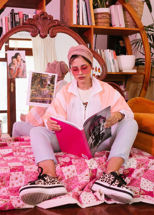 an image of a woman sitting on the floor reading a magazine with oink sunglasses on