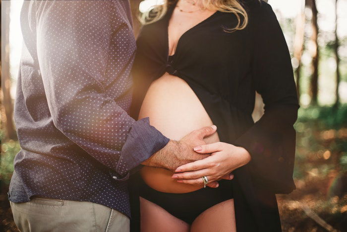 A couple posing with a partner's hand on her belly for pregnant boudoir photography