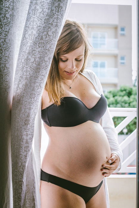 A woman posing in lingerie by a curtain for pregnant boudoir photography