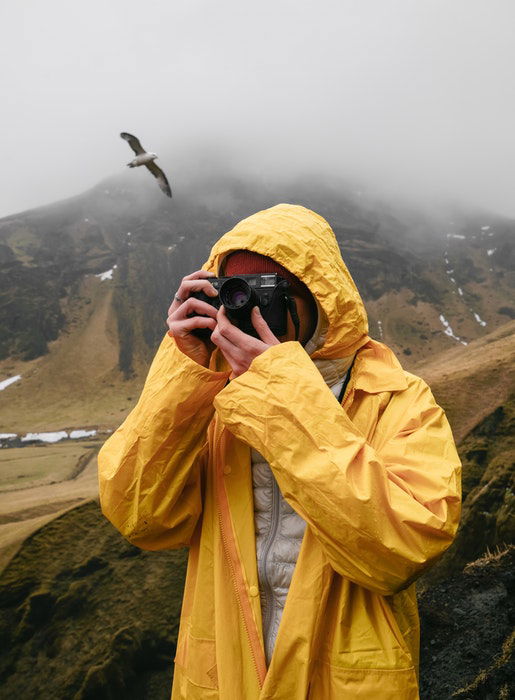 A photographer in yellow rain jacket shooting on a rainy day in the mountains with a bird behind him