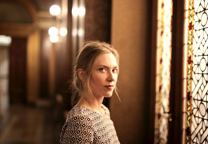 A woman is standing in an entryway with stained glass windows in front if her.