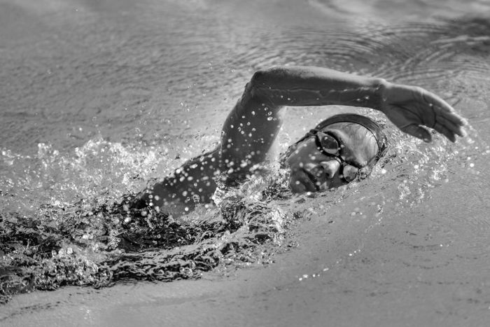 Black and white image of a woman swimming in a pool.