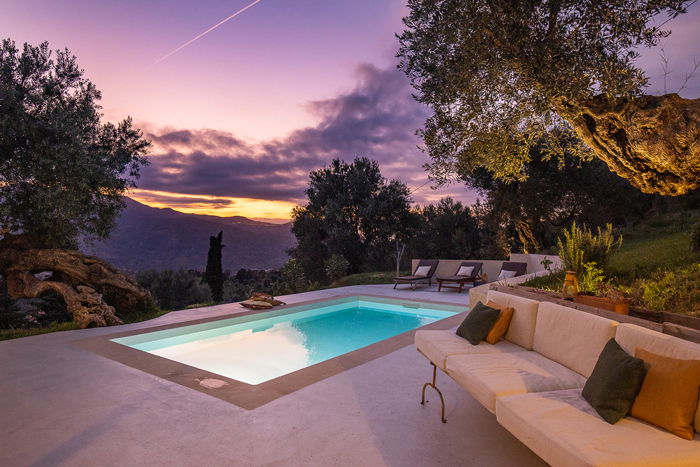 a twilight shot of a house exterior with pool and sofa against a pink sky