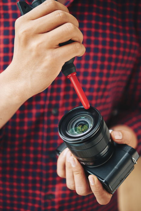 A man cleaning his camera lens with a black and red blower and lens cleaning solution. 