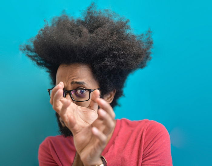 portrait of a young black man with glasses looking through his hands