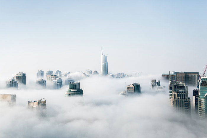 a photograph of city skyscrapers peaking through the clouds