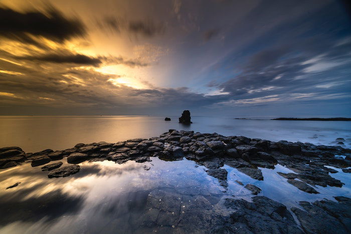 a long exposure photograph of clouds above water and rocks