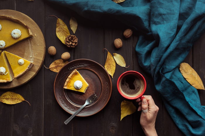 Pumpkin pie and a hot beverage on a table with autumn leaves walnuts and pinecones