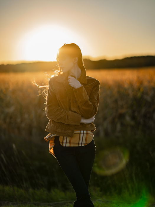 an image of a woman posing in a meadow with setting sun behind her