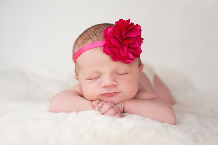 A baby girl with a flower on her head is lying on a fluffy bed.