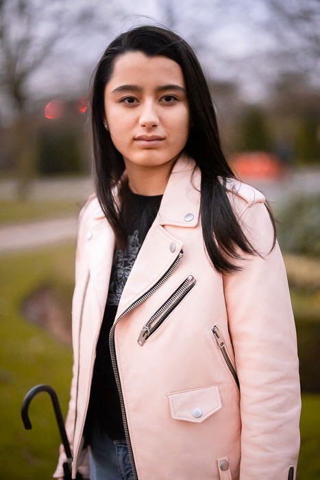 A woman posing outdoors with a pink jacket.