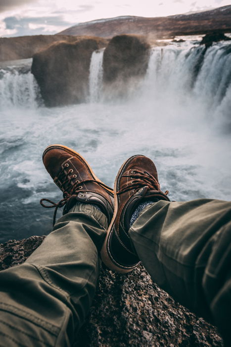 a closeup image of a mans legs and shows against a large waterfall