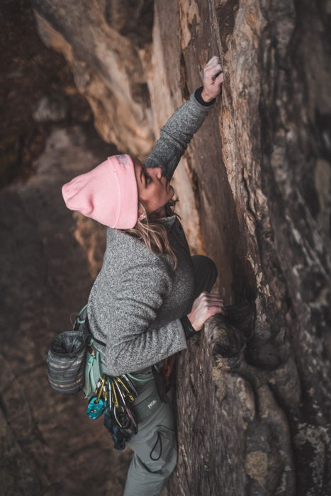 adventure photography of a woman in a pink hat climbing up the side of a mountain