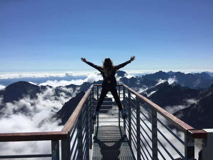 an image of a woman at the summit of a mountain looking beyond the clouds