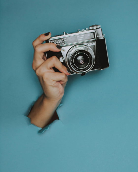 A persons hand holds a camera in front of a blue background.