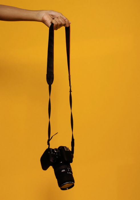 A DSLR camera with a strap hanging against a yellow background.