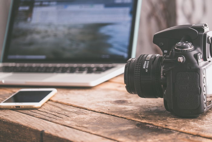 A DSLR camera sitting on a wooden surface next to an open laptop.