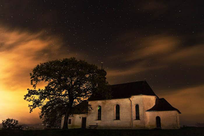 Long exposure night photography of a small church and a tree under the night sky