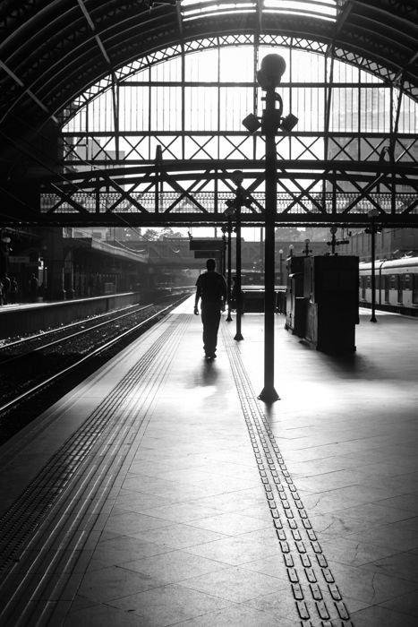 black and white image of a man walking on a platform in a train station