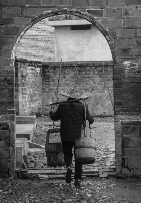 black and white image of a man in a cap walking through an arch