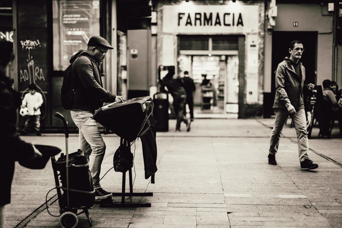 A man is playing an upright piano on a busy city street.