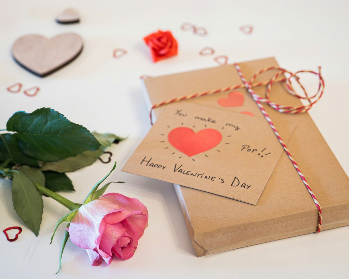 A still life of a rose, gift, and heart shapes on a table as a Valentines day photoshoot idea