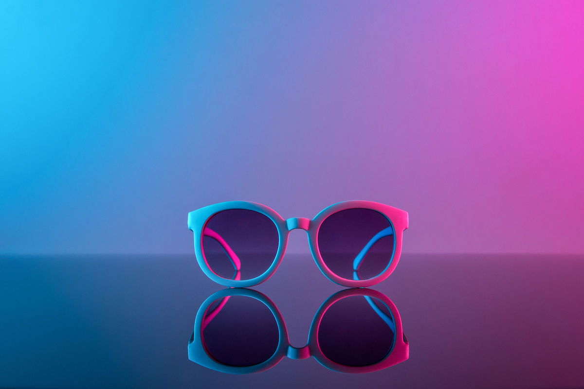 Stylish sunglasses shot using pink and blue abstract colored lighting with a reflection on a glass surface