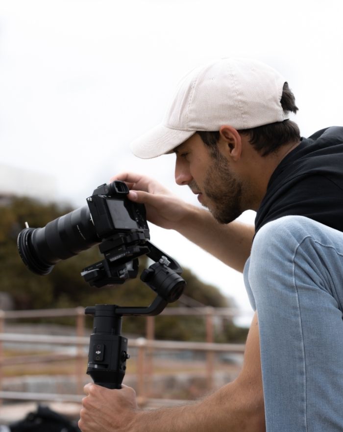 Man in black shirt and jeans looking through a Dslr Cameras viewfinder