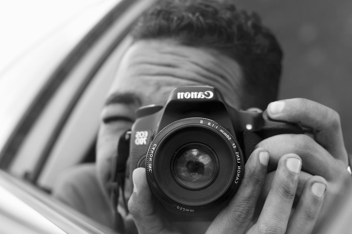 A person taking a selfie in a car mirror with a nifty fifty lens