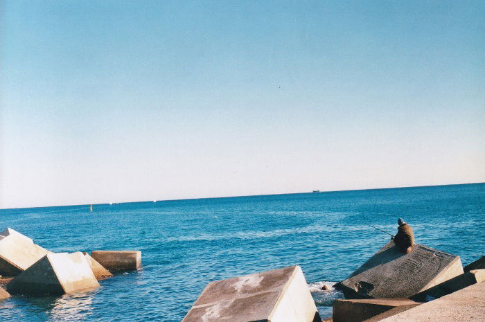 Sea fisherman sitting on a large concrete block