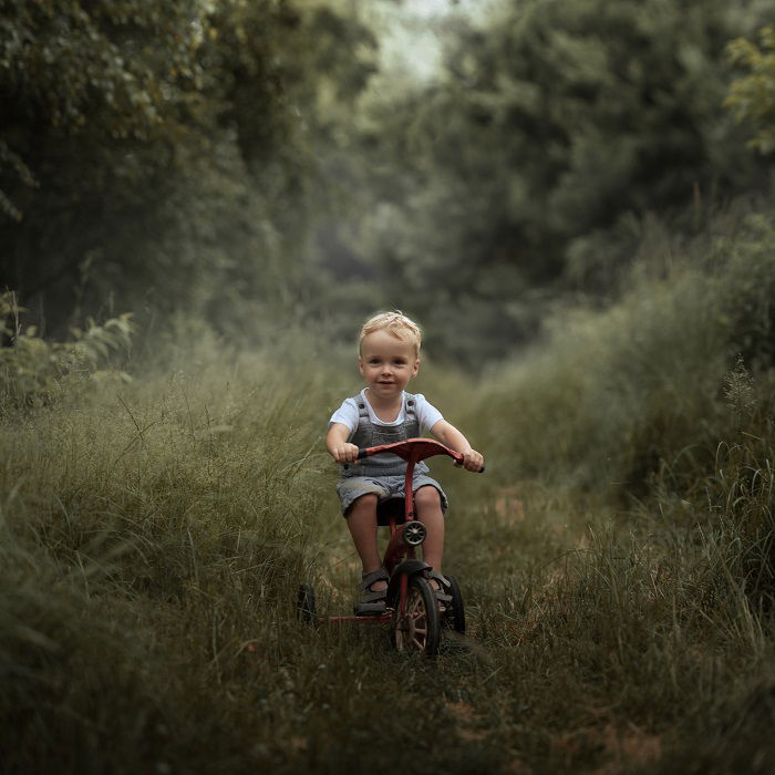 child riding a tricycle through a woodland trail