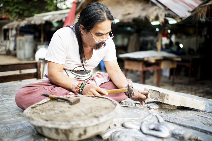 A man working with a hammer in an outdoor artist workshop in Thailand