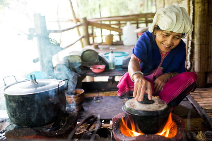 An environmental portrait of a Karen woman cooking on am outdoor patio with pots over a fire