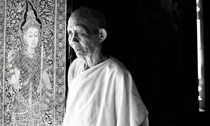 A black and white environmental portrait of a Buddhist nun with a carved relief in the background