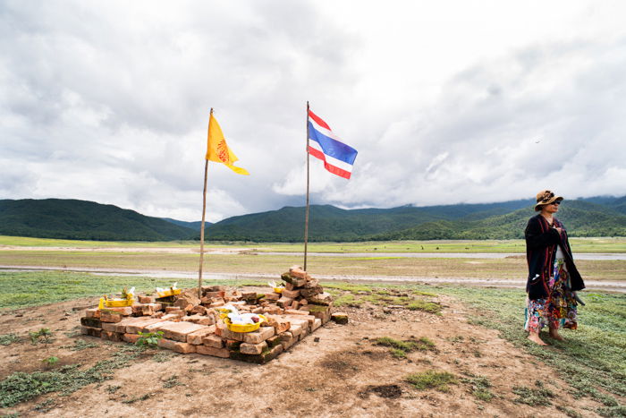 An environmental portrait of a woman standing beside a make shift Buddhist shrine in a a dry lake bed in Chiang Mai, Thailand