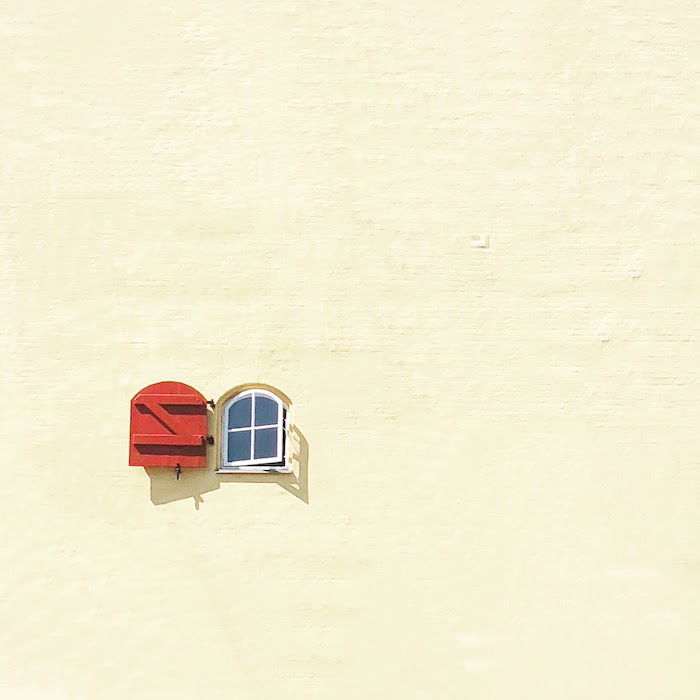 Minimalist architecture photography: A minimalist image with a small window with an open red shutter on a large blank wall