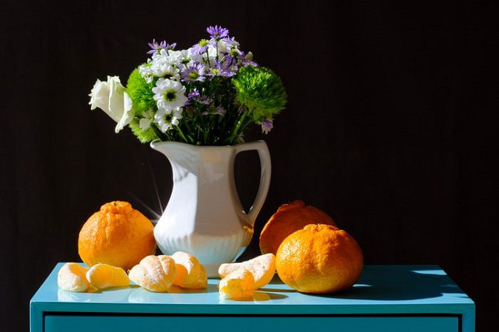 still life photo of flowers in a jug and oranges