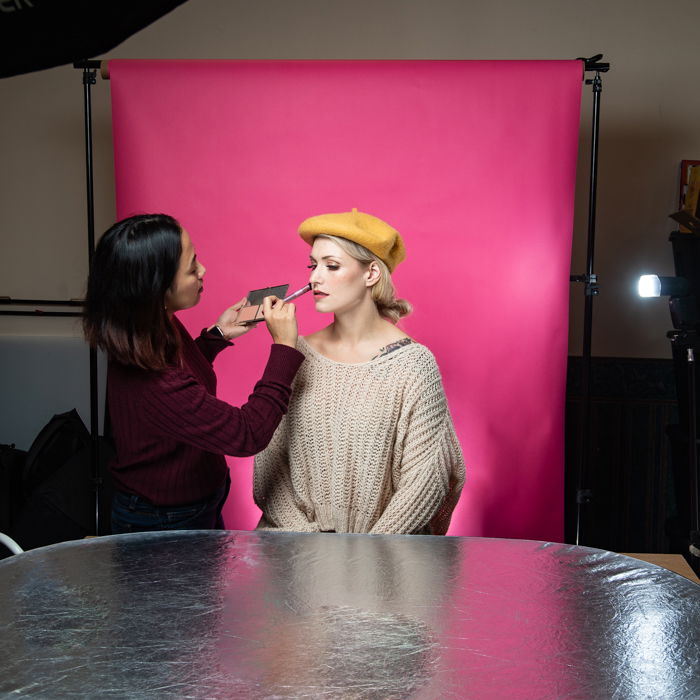 A woman applying makeup on a model in a small studio