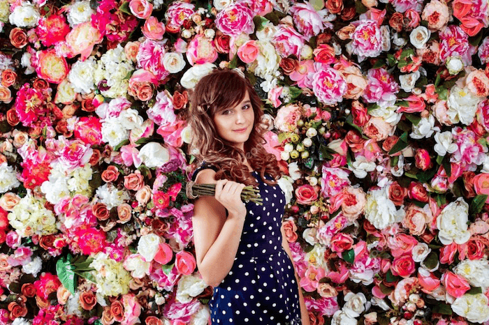 an image of a young woman holding a bouquet standing against a flower well