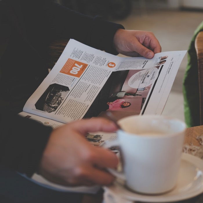 photograph of a person reading a local newspaper while holding a cup of coffee