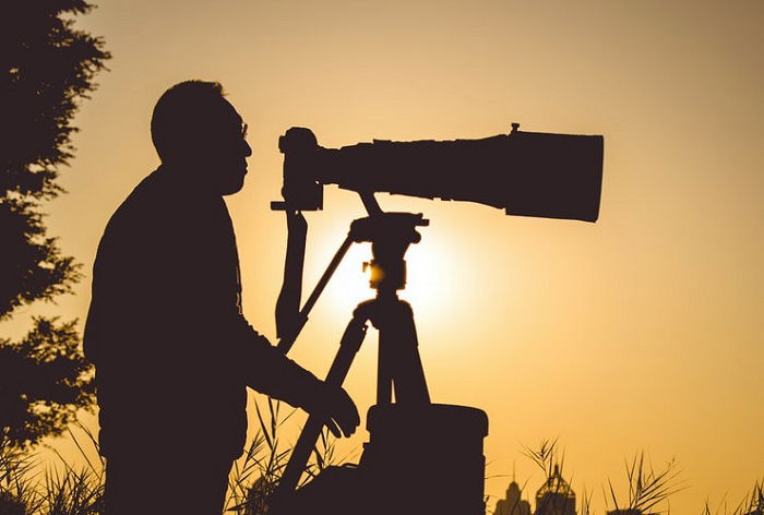 image of a man using a telephoto lens on a tripod with low sun in the background