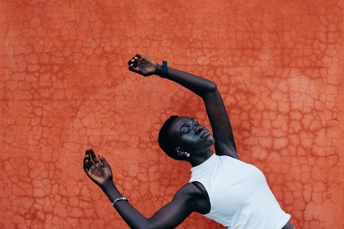 A conceptual editorial portrait of a woman falling back against an orange, textured background