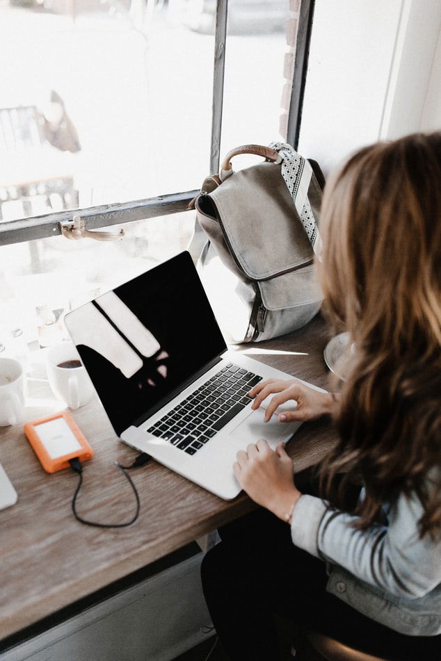 woman using a MacBook and an external drive as a way to store photos