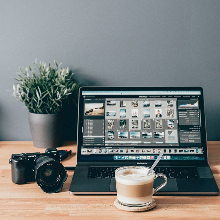 laptop showing photos that have been uploaded from a camera behind a cup of coffee