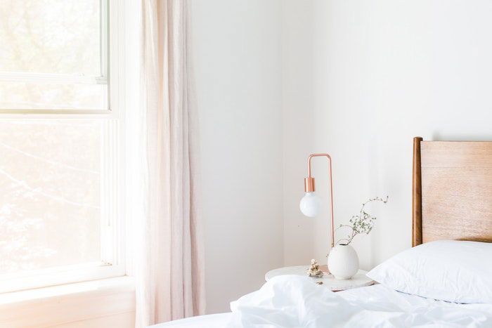 A bright white room with a bed window and night stand shot by a real estate photographer