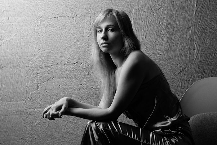 A black and white portrait of a woman sitting with soft light bouncing off the wall behind her